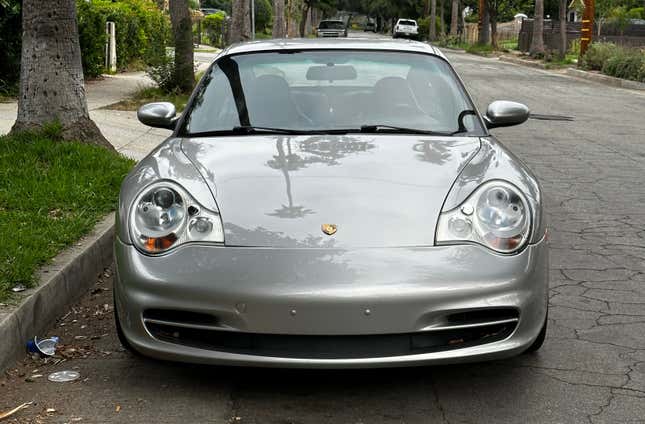 A silver Porsche 911 is parked on a street. Palm trees are reflected in the hood.