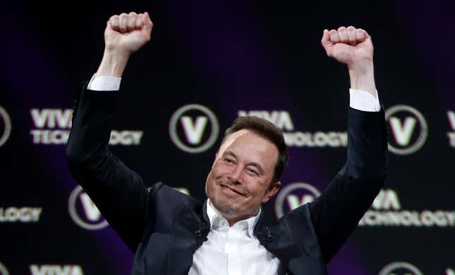 Elon Musk in a suit with no tie holding his hands up over his head. Background is the logo for the Viva Technology Conference. 